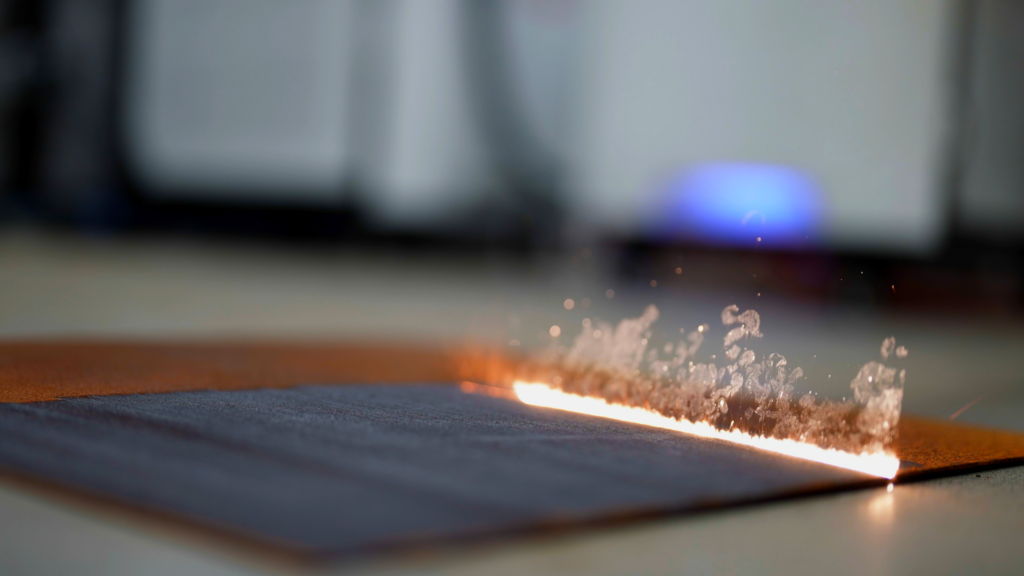 Nahaufnahme eines Lasers, der eine Metallplatte reinigt und dabei Funken und Ablagerungen entfernt.